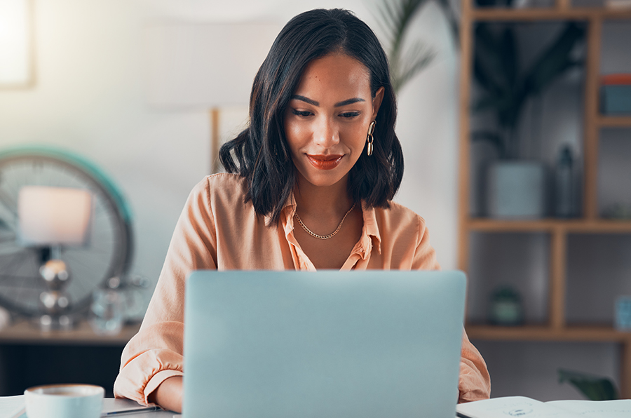 A woman in a peach outfit working on AMS Solutions on a laptop