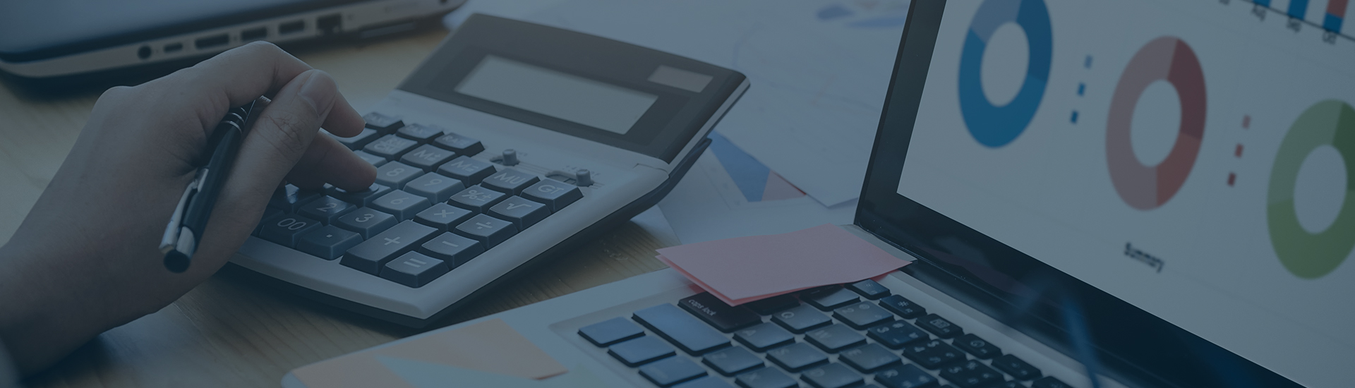 A view of a hand of a person working on a calculator and a laptop